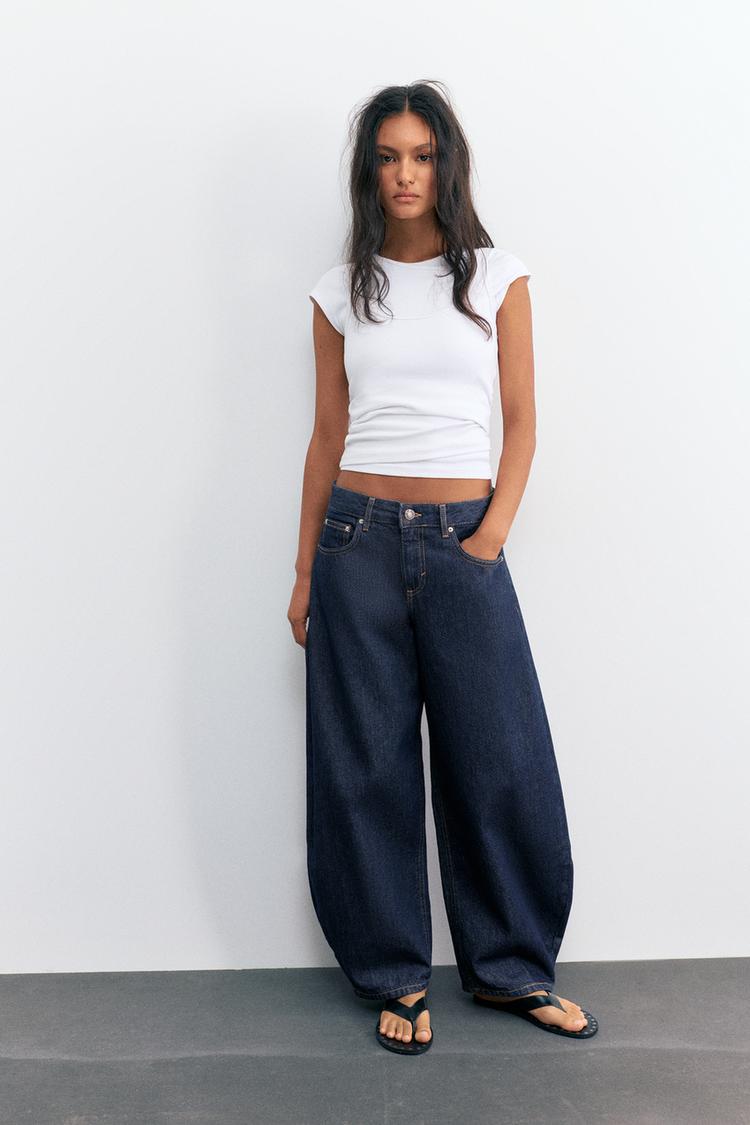 Conjunto de camiseta blanca de manga corta, jeans barrel azul marino de tiro bajo con bolsillos frontales y trabillas, y sandalias negras.