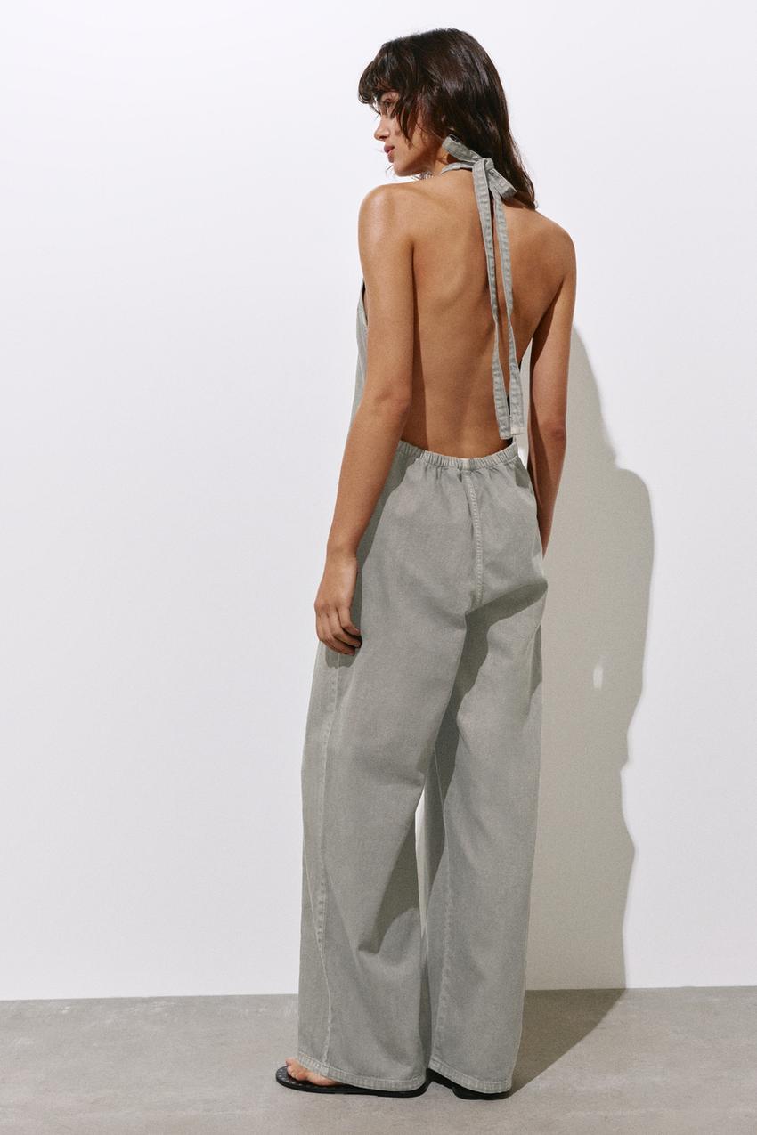 Taupe grey long jumpsuit with open back, flowing design and side pockets.