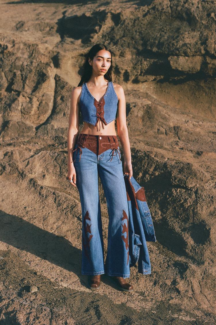 Conjunto de chaleco azul claro con cierre de cordón y pantalones vaqueros con detalles marrones y estampado en las piernas.