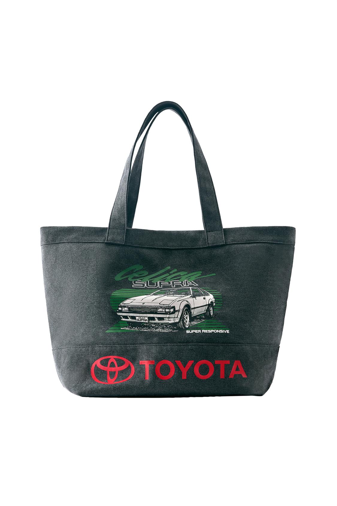 Kulplu antrasit alışveriş çantasının önden görünüşü. "Celica", "SUPRA", "SUPER RESPONSIVE" yazıları ve kırmızı "TOYOTA" logosu içeren araba baskılı.