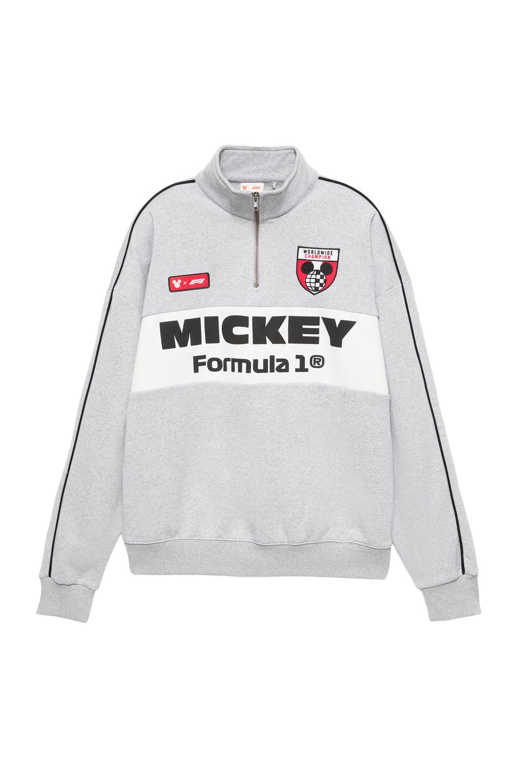 Yarım fermuarlı gri sweatshirt'ün önden görünümü. 'MICKEY Formula 1®' ve 'WORLDWIDE CHAMPION' yazıları, beyaz şerit ve siyah biye detayları.